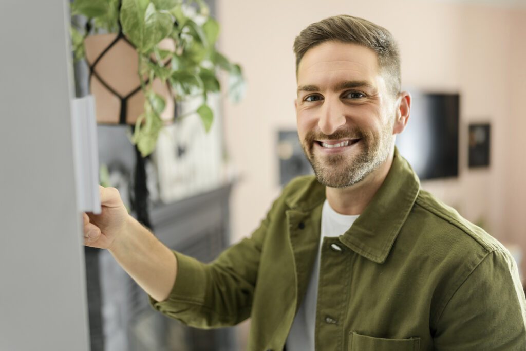 Jeune homme souriant en train de régler la température du thermostat de son système de chauffage central résidentiel.
