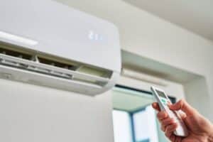 Plan rapproché d'une thermopompe murale et de la main d'une personne ajustant la température à l'aide d'une manette