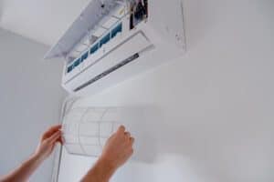 Bras d'une personne retirant le filtre à air pour nettoyer la thermopompe murale.