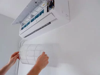 Bras d'une personne retirant le filtre à air pour nettoyer la thermopompe murale.