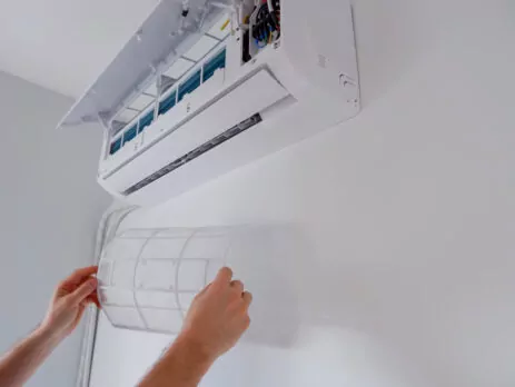 Bras d'une personne retirant le filtre à air pour nettoyer la thermopompe murale.