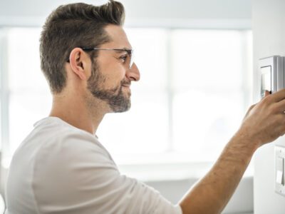Un homme programme la température désirée sur le thermostat après l'installation de sa thermopompe centrale