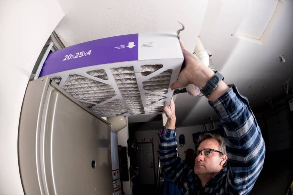 A man replaces the furnace filter, following the direction of the filter