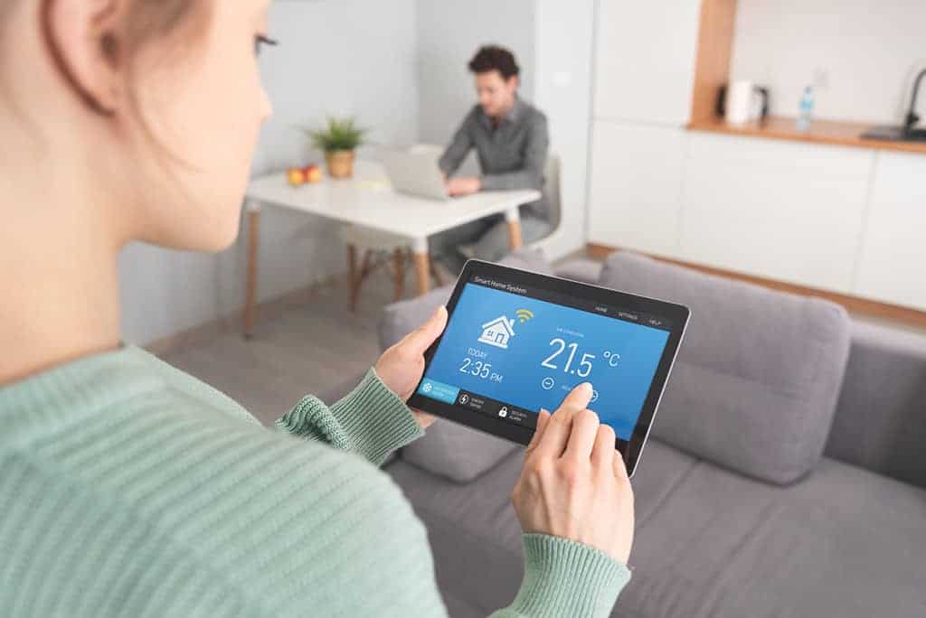 Jeune femme programmant la température de son thermostat à l'aide de sa tablette électronique