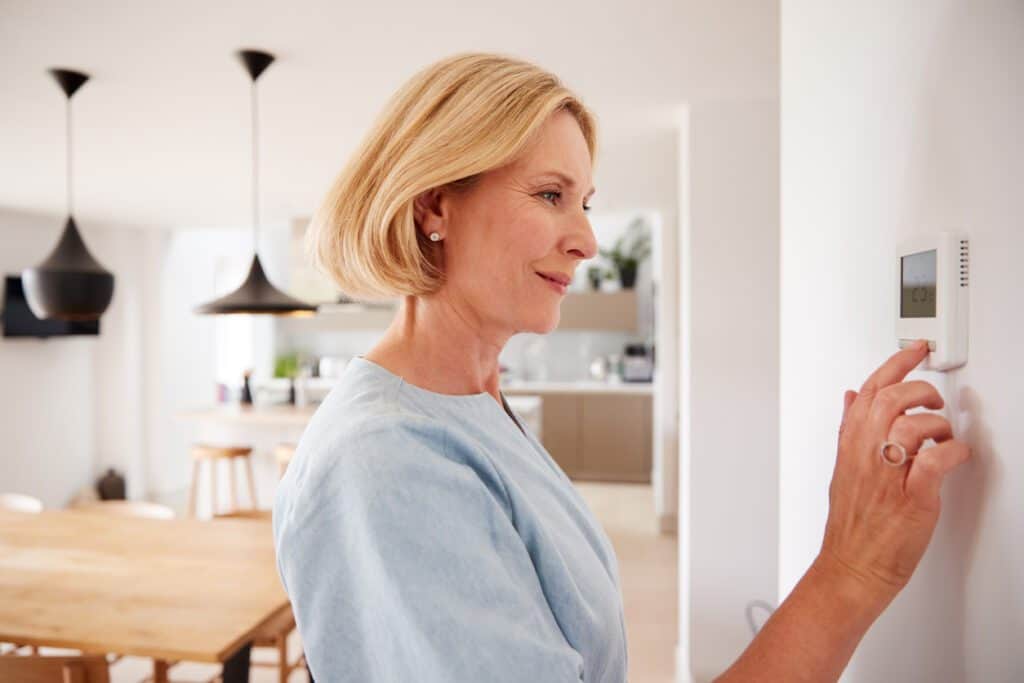 A woman adjusts the temperature on her electronic heat pump thermostat mounted on the dining room wall