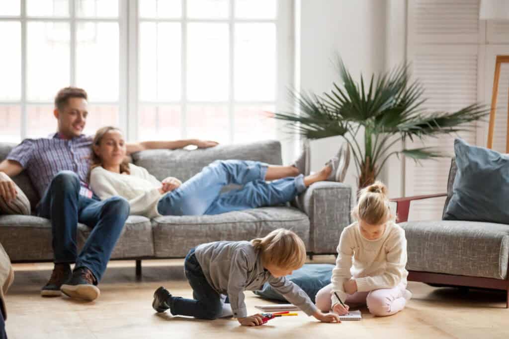 Famille vivant un moment de détente au salon. Les parents relaxent sur le canapé et les enfants dessinent, assis au sol.