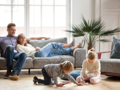 Famille vivant un moment de détente au salon. Les parents relaxent sur le canapé et les enfants dessinent, assis au sol.