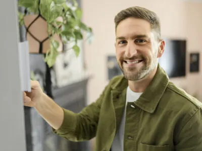 Jeune homme souriant en train de régler la température du thermostat de son système de chauffage central résidentiel.