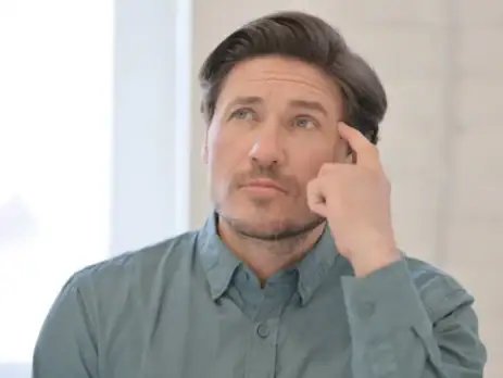 Portrait of a pensive middle-aged man, finger to his temple, wondering why his heat pump runs all the time.