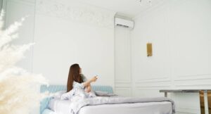 Jeune femme assise sur son lit qui démarre son air climatisé.
