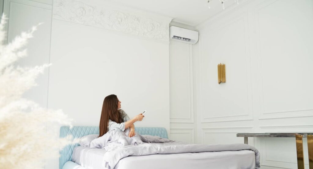 Young woman sitting on her bed starting up her air conditioner.