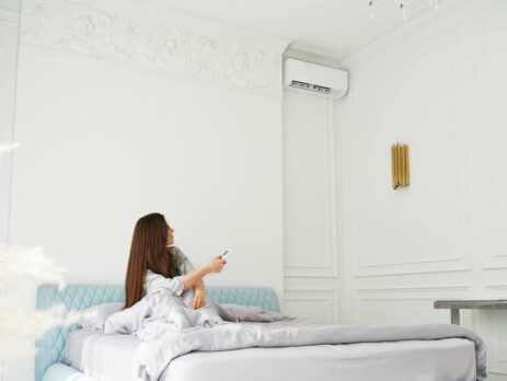 Young woman sitting on her bed starting up her air conditioner.