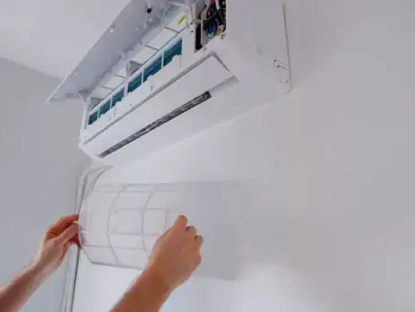 Woman repositioning the filter on her wall-mounted heat pump