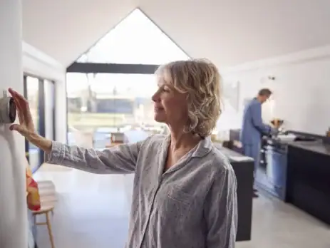 Woman adjusting the thermostat on her electric furnace when she wakes up