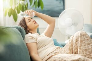 Jeune femme qui tente de se rafraîchir avec un ventilateur, car son air climatisé ne refroidit plus.